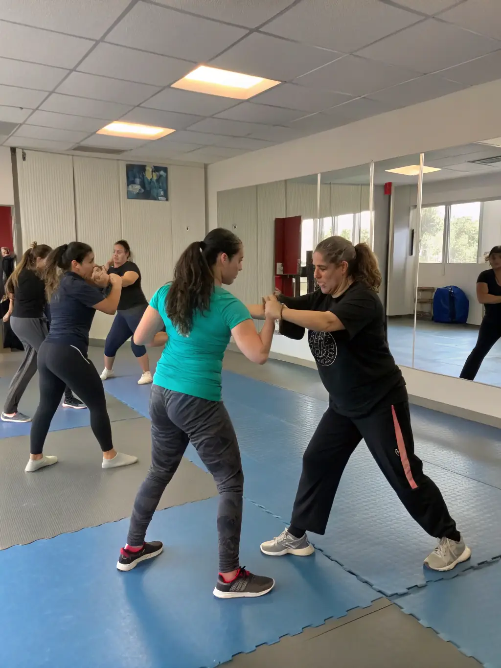 A diverse group of adults and teenagers practicing self-defense techniques in a well-lit gymnasium, focusing on wrist escapes and blocks, demonstrating SMA 18's commitment to practical self-defense skills.